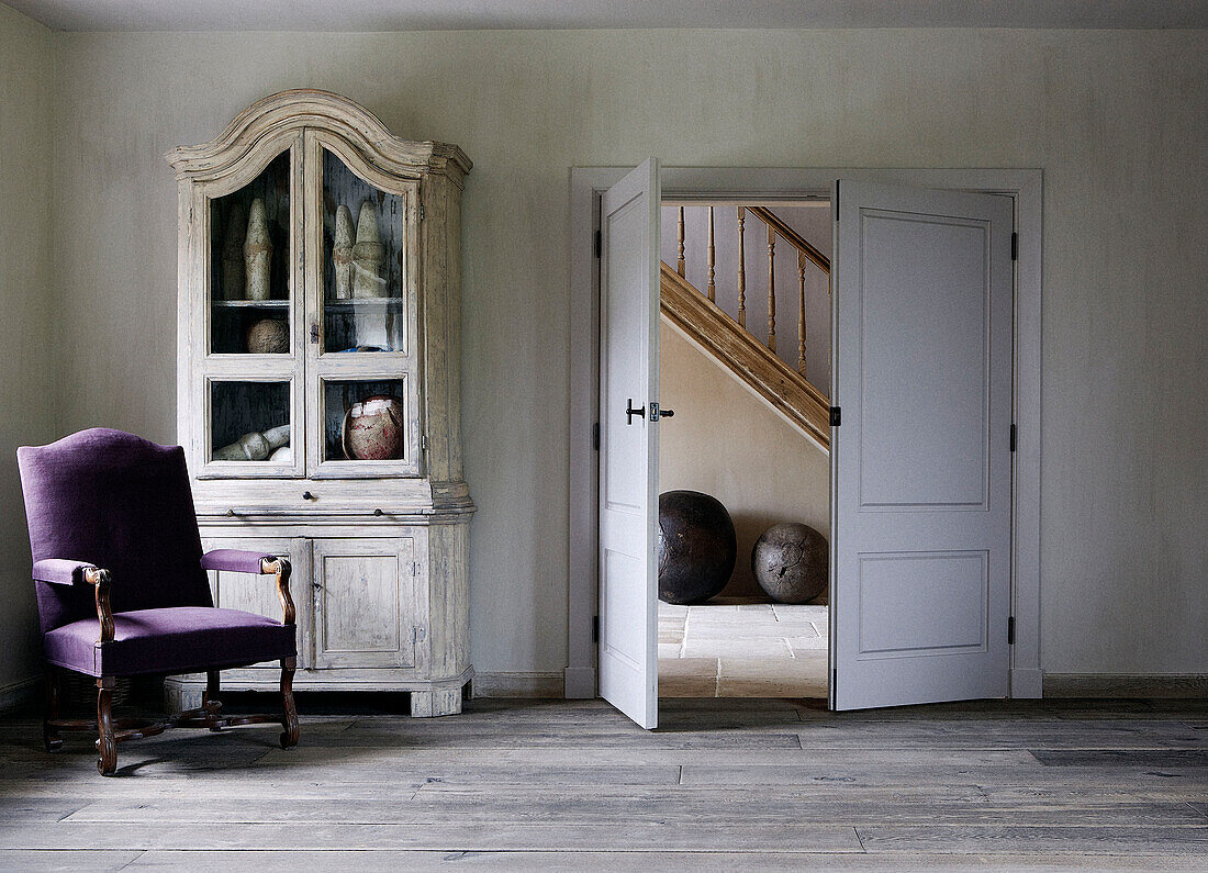 Purple armchair and glass fronted cabinet with double doors in country home