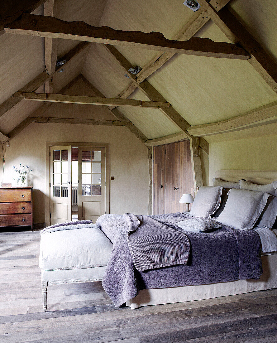 Fliederfarbene Bezüge auf einem Bett mit Dachschräge in einem Landhaus
