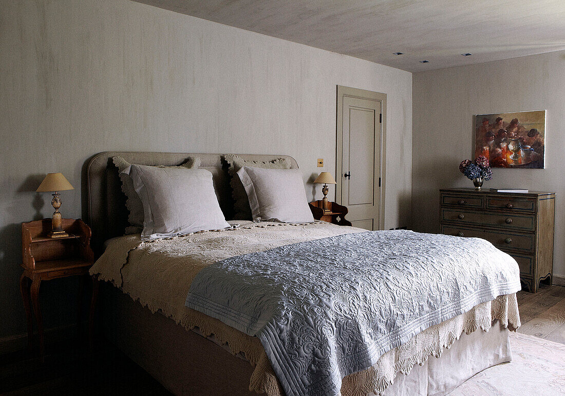 Bedroom of country home with embroidered and lace bed covers in light blue and cream