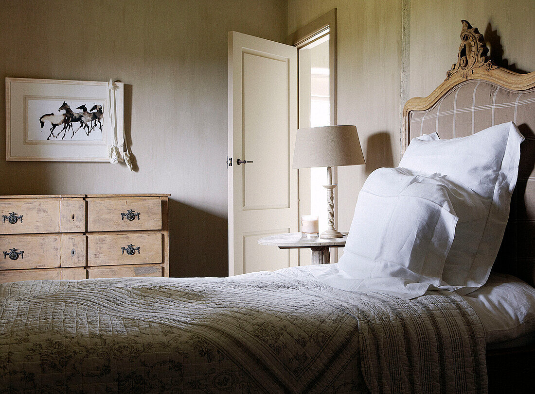 Equestrian artwork above wooden chest of drawers in bedroom of country home