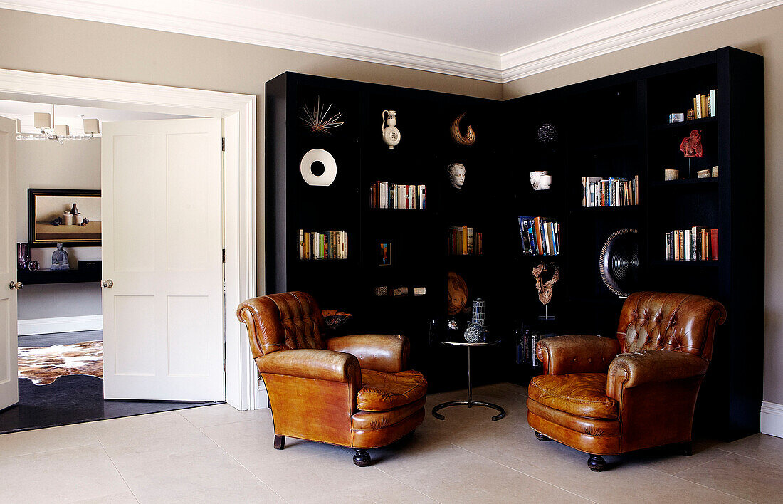 Brown leather armchairs and black bookcase with ornaments