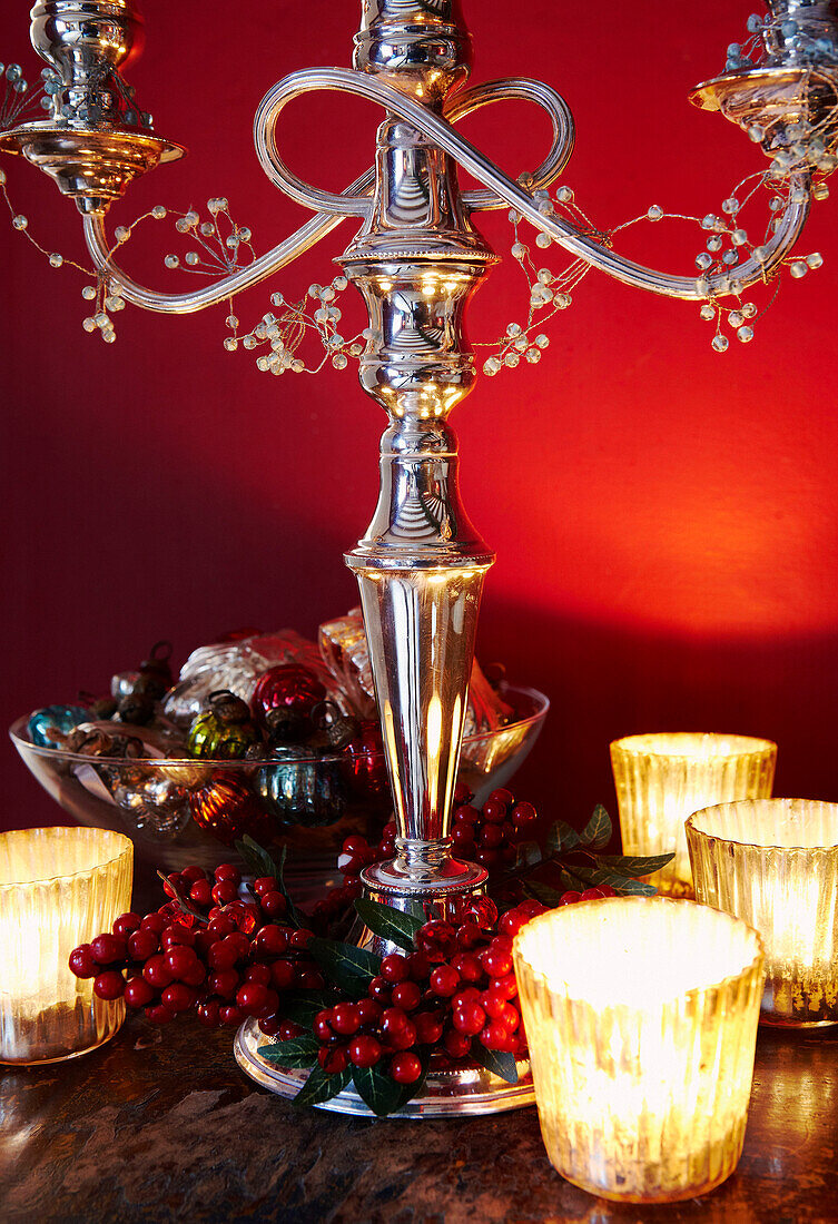 Silberner Kerzenständer und brennende Kerzen mit Weihnachtssüßigkeiten in einer Schale