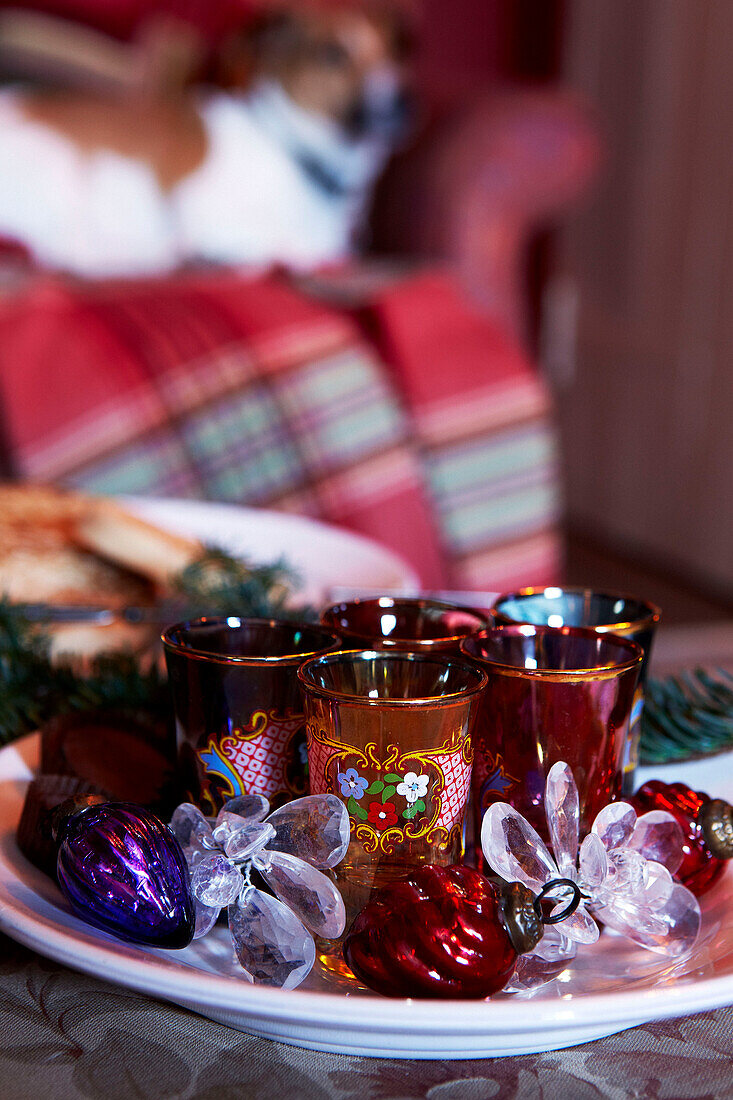 Farbige Teelichthalter und gläserner Weihnachtsschmuck auf einem Teller