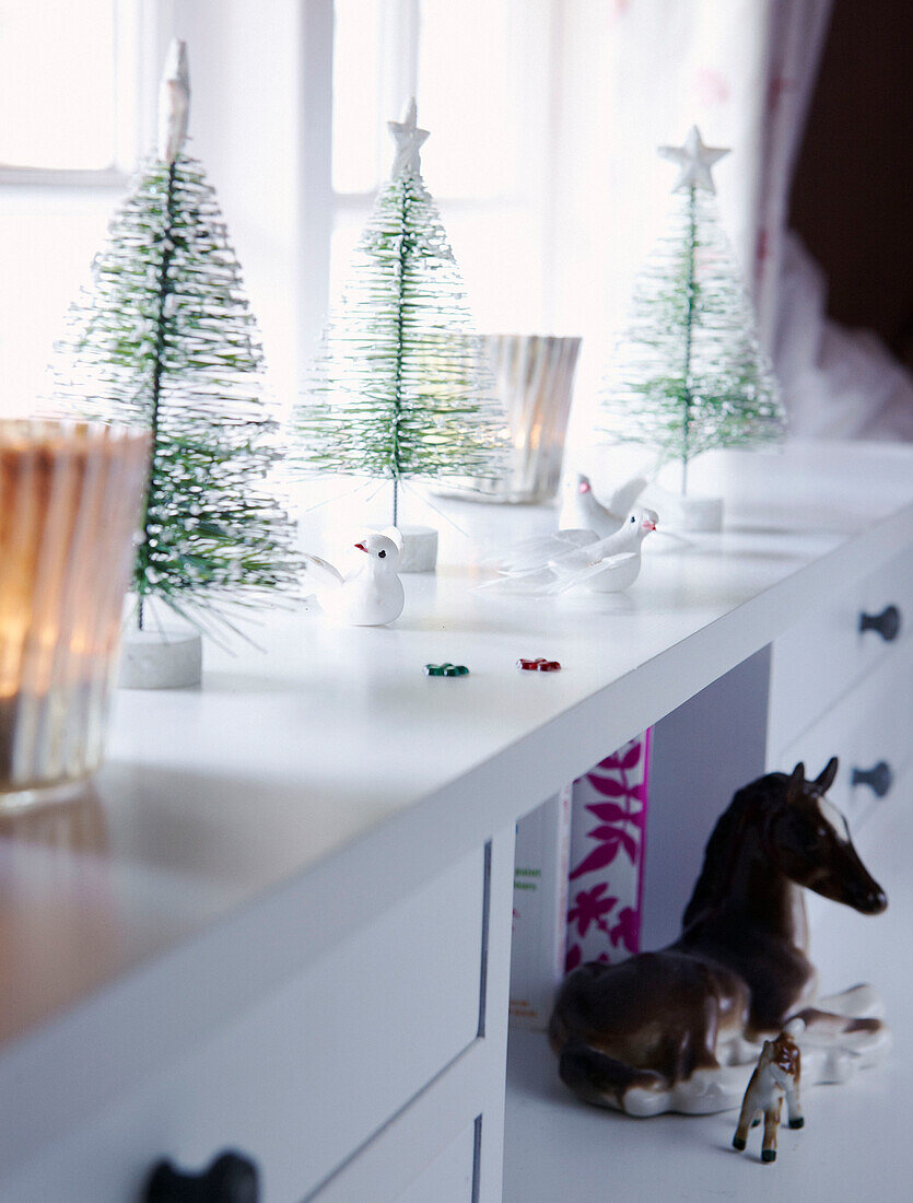 Weihnachtsbäume und Vögel auf weißem Schreibtisch am Fenster mit Spielzeugtieren