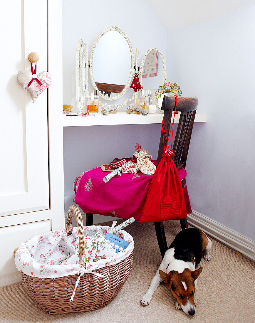 Dog sleeping next to basket under chair at dressing table with mirror