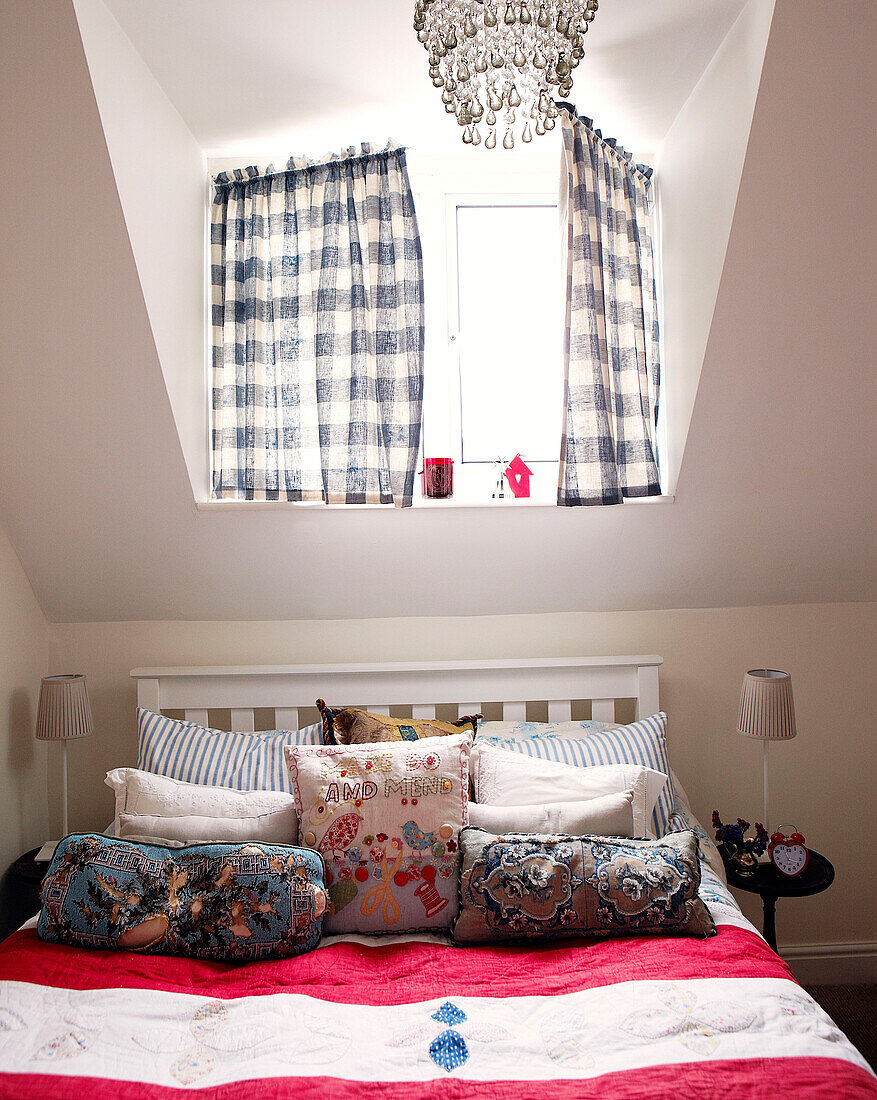 Blau-weiß karierte Vorhänge über dem Bett mit rosa gestreiftem Bezug und einer Auswahl an Kissen