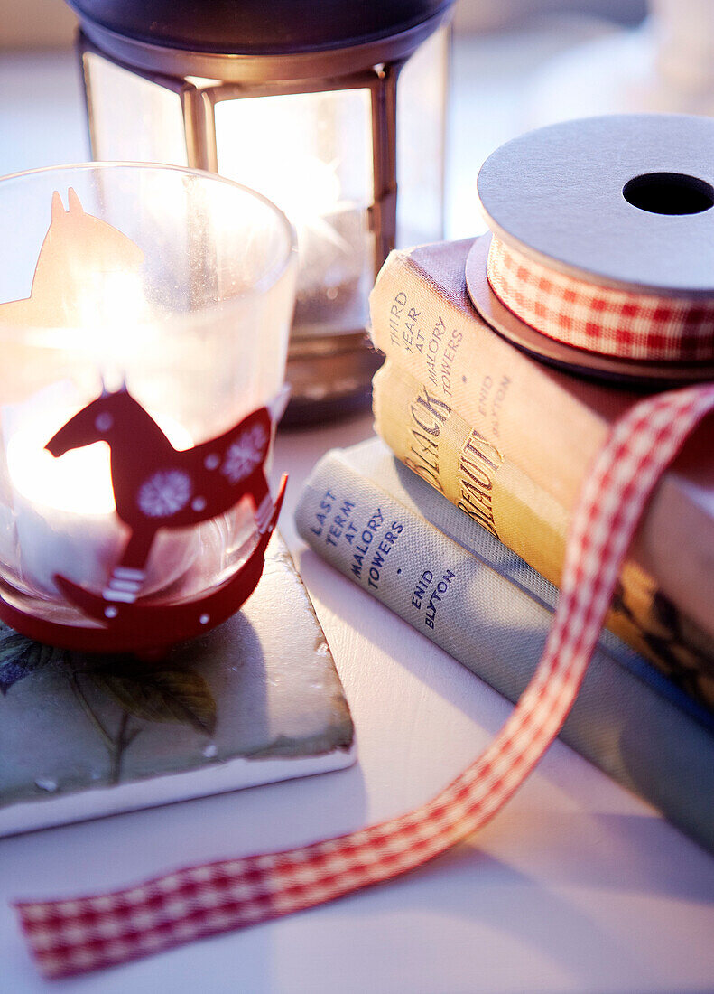 Hard backed books and checked ribbon with lit candle and lantern