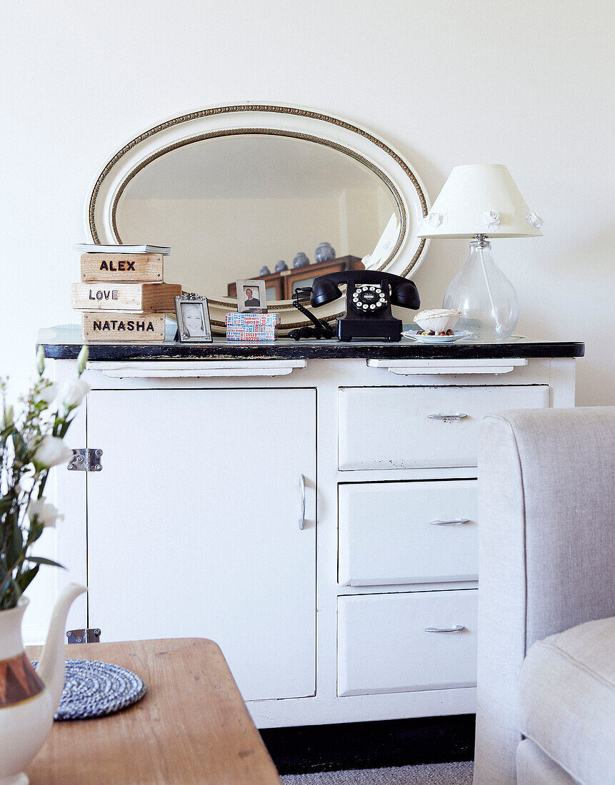 Rotary dial telephone and oval shaped mirror on white side unit