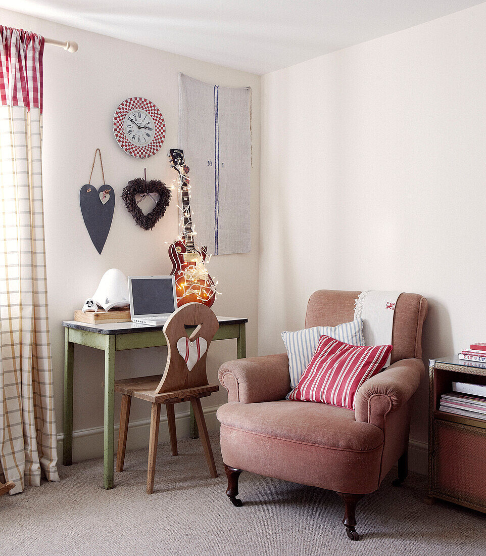Armchair and desk in corner of room with heart shaped wall ornaments and electric guitar