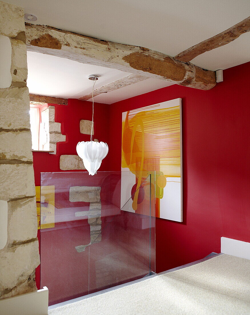 Glass partition on red staircase landing with modern art in renovated Cotswolds mill house England UK
