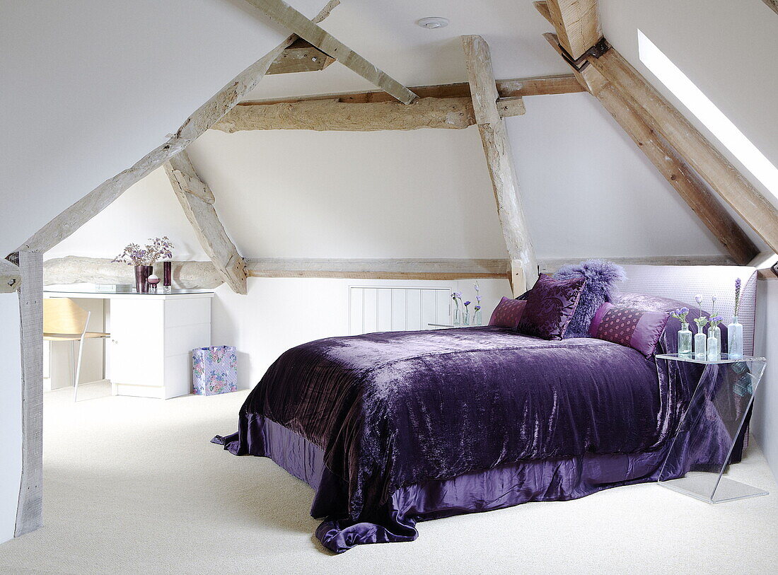 Purple bedspread on bed in beamed attic conversion of renovated Cotswolds mill house England UK