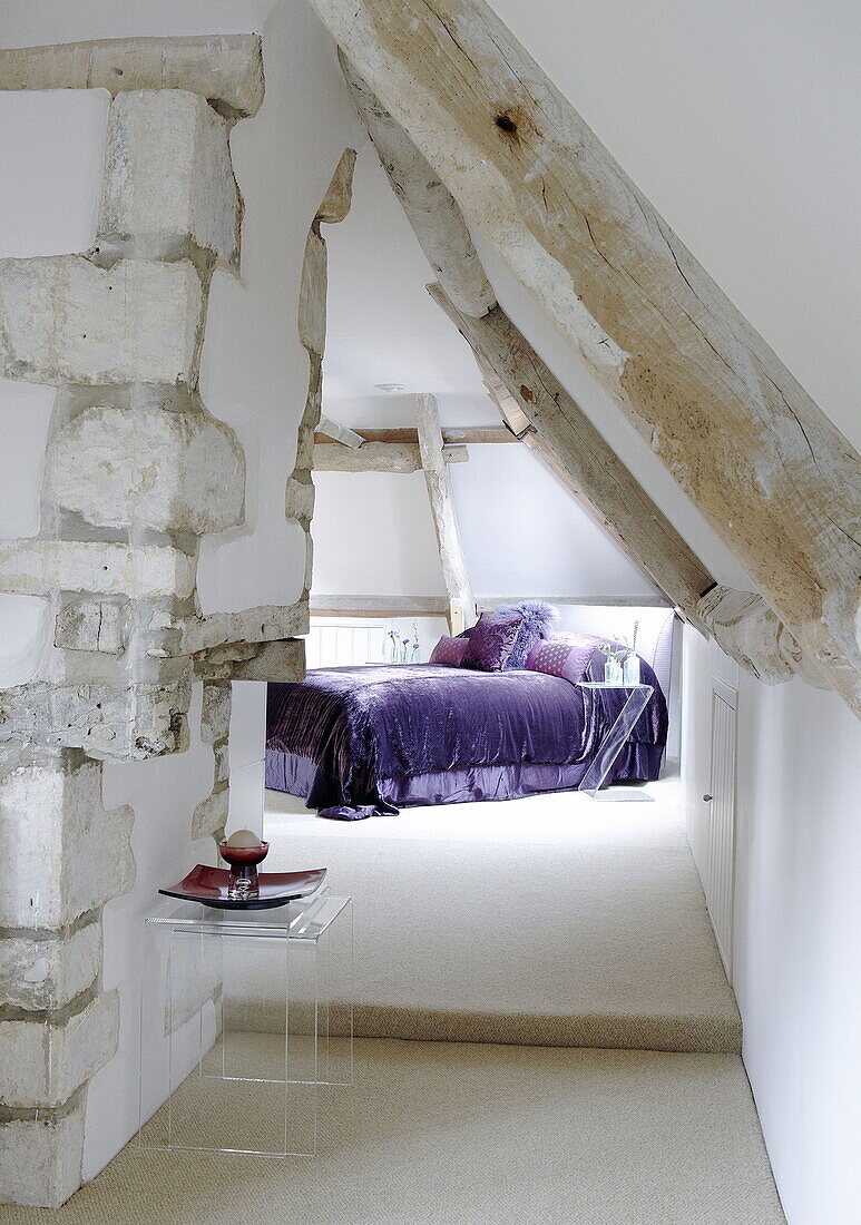Bett mit violetten Bezügen im Dachgeschoss eines renovierten Mühlenhauses in den Cotswolds England UK