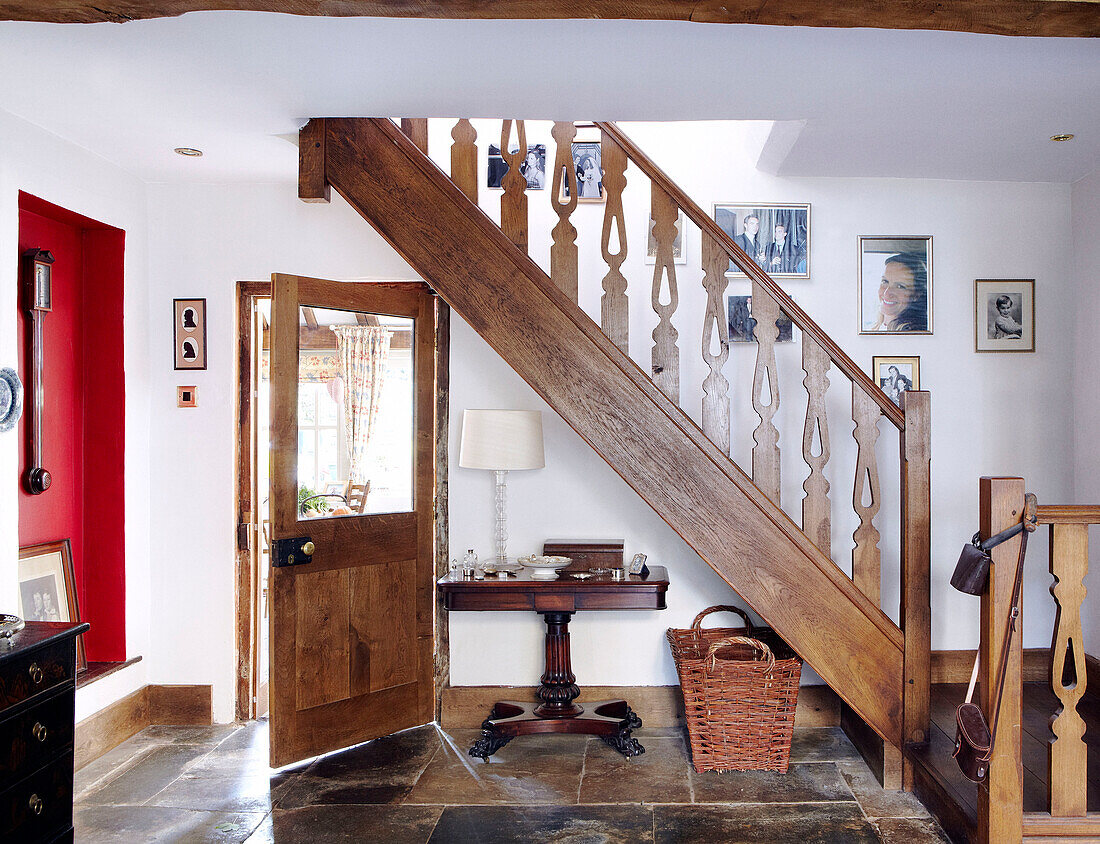 Family photographs hang on staircase with wooden banister in flagstone entrance foyer