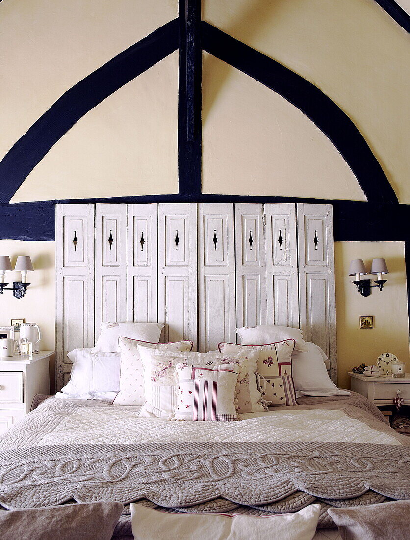 Navy blue painted timber frame above salvaged shutters headboard in bedroom of Forest Row farmhouse Surrey England UK