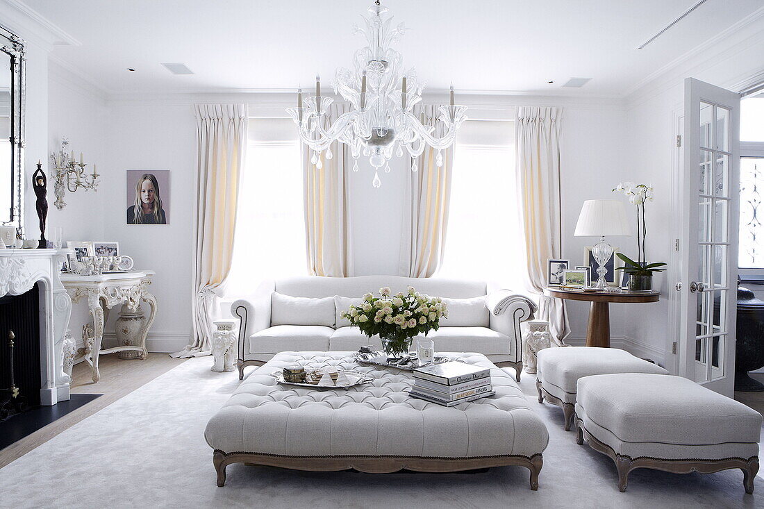 Cut flowers and books on white ottoman below glass chandelier in living room of London home UK