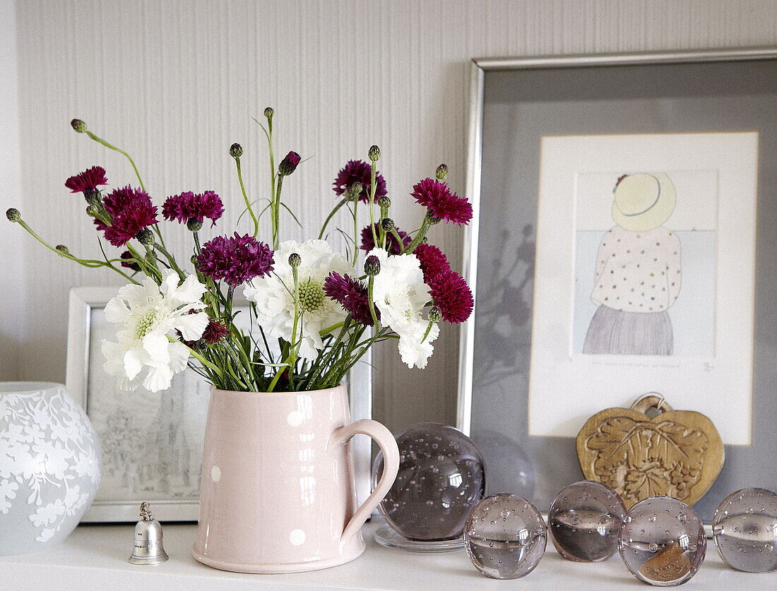 Jug with cornflowers and widow flower and glass paperweights with artwork in a house in London UK