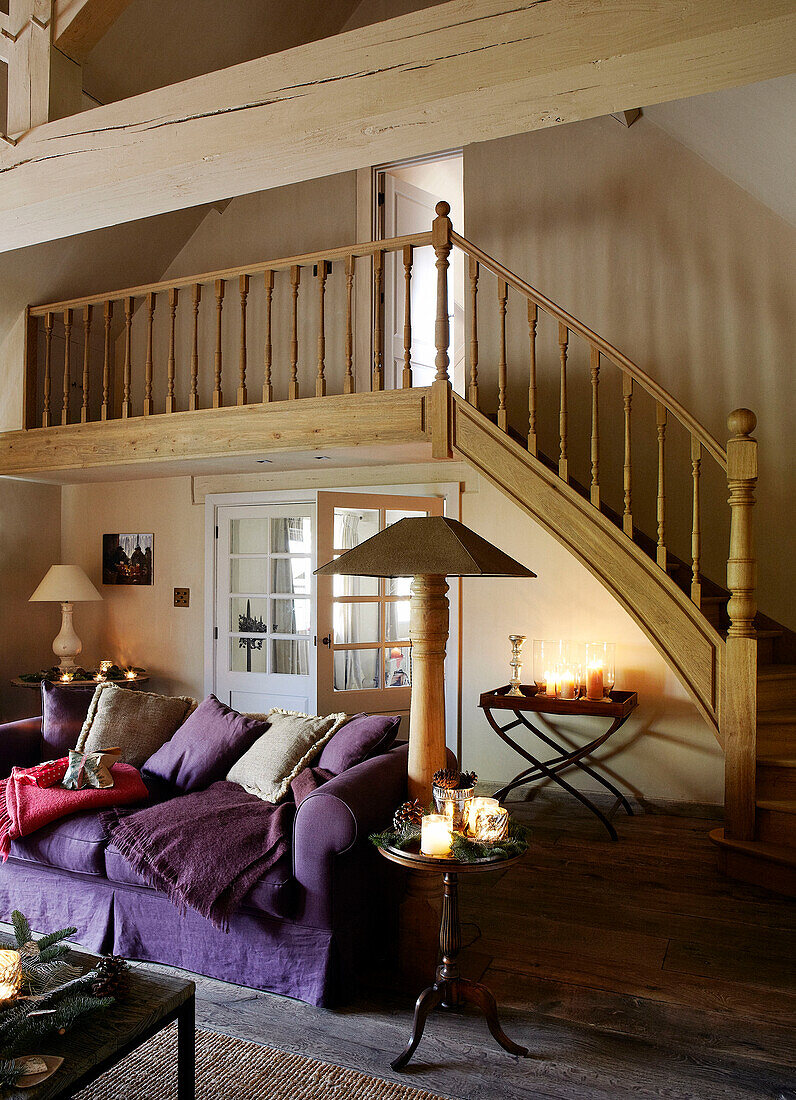 Purple sofa and lit candles in open plan living room with wooden staircase in festive Oxfordshire home, England, UK