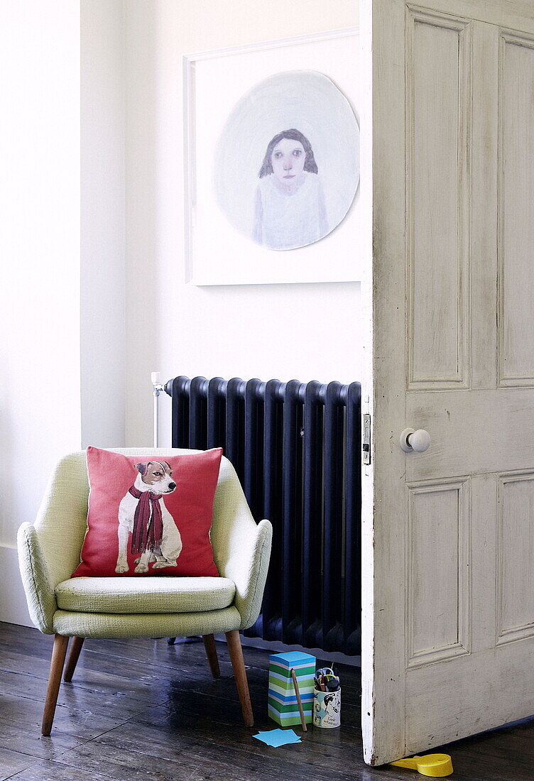 Vintage-Stuhl neben einem Kunstwerk über dem Heizkörper in einem Einfamilienhaus in London UK
