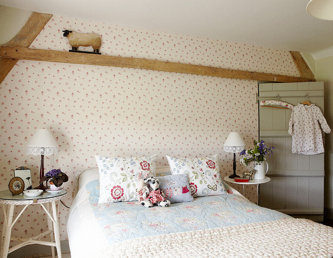 Artwork on bedroom wall with floral embroidered cushions and bedside table in Oxfordshire farmhouse, England, UK