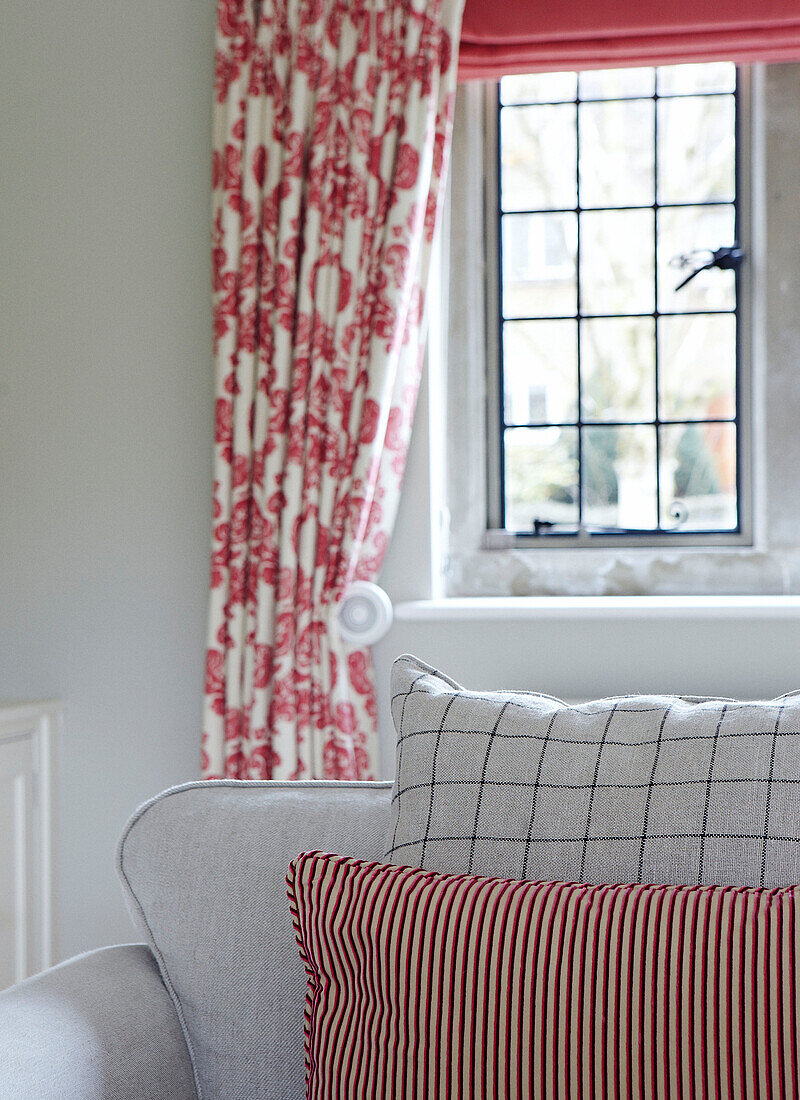 Striped and checked cushions on sofa in Oxfordshire living room with floral curtains, detail, England, UK