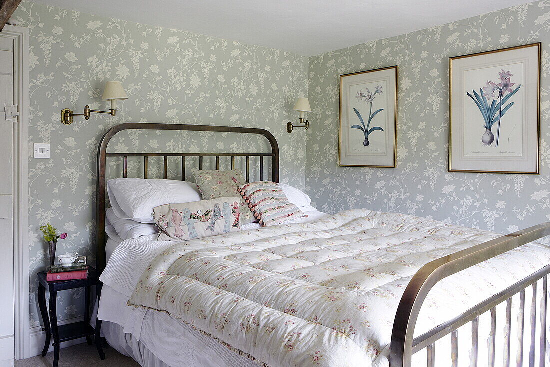 Metallgerahmtes Bett mit botanischen Drucken in einem Schlafzimmer mit Blumenmuster in einem Haus in Oxfordshire, England, UK
