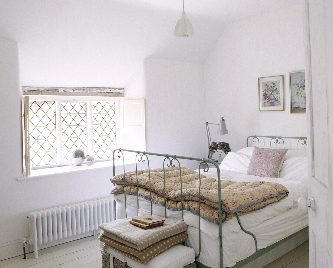 Metal framed bed in room with leaded window, Oxfordshire cottage, England, UK