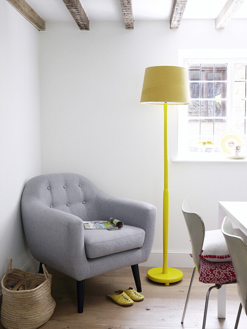 Grey armchair with yellow standard lamp and basket in corner of contemporary Oxfordshire cottage, England, UK