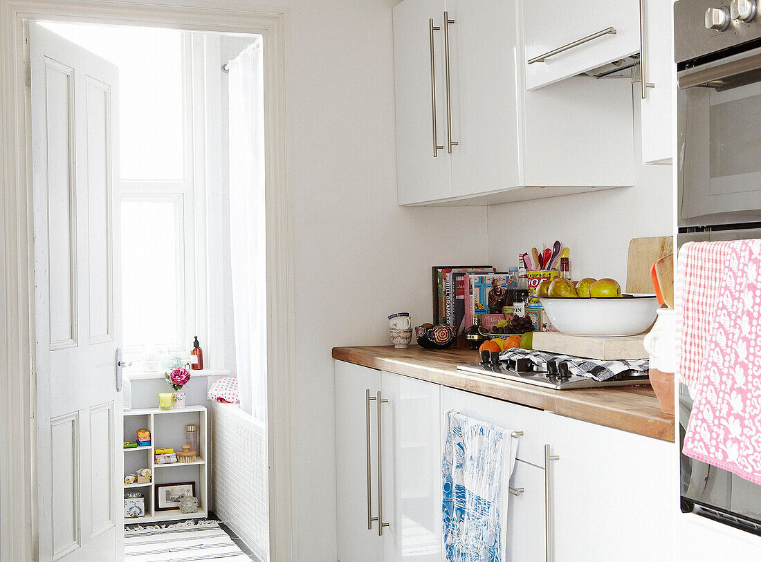 Blick von der Küche mit weißen Einbauschränken und hölzerner Werkbank durch die Tür zum Badezimmer in einem Haus in Hastings, East Sussex, UK