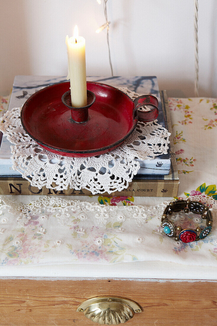 Lit candle on a red candlestick with lace doilly in contemporary home, Hastings, East Sussex, UK