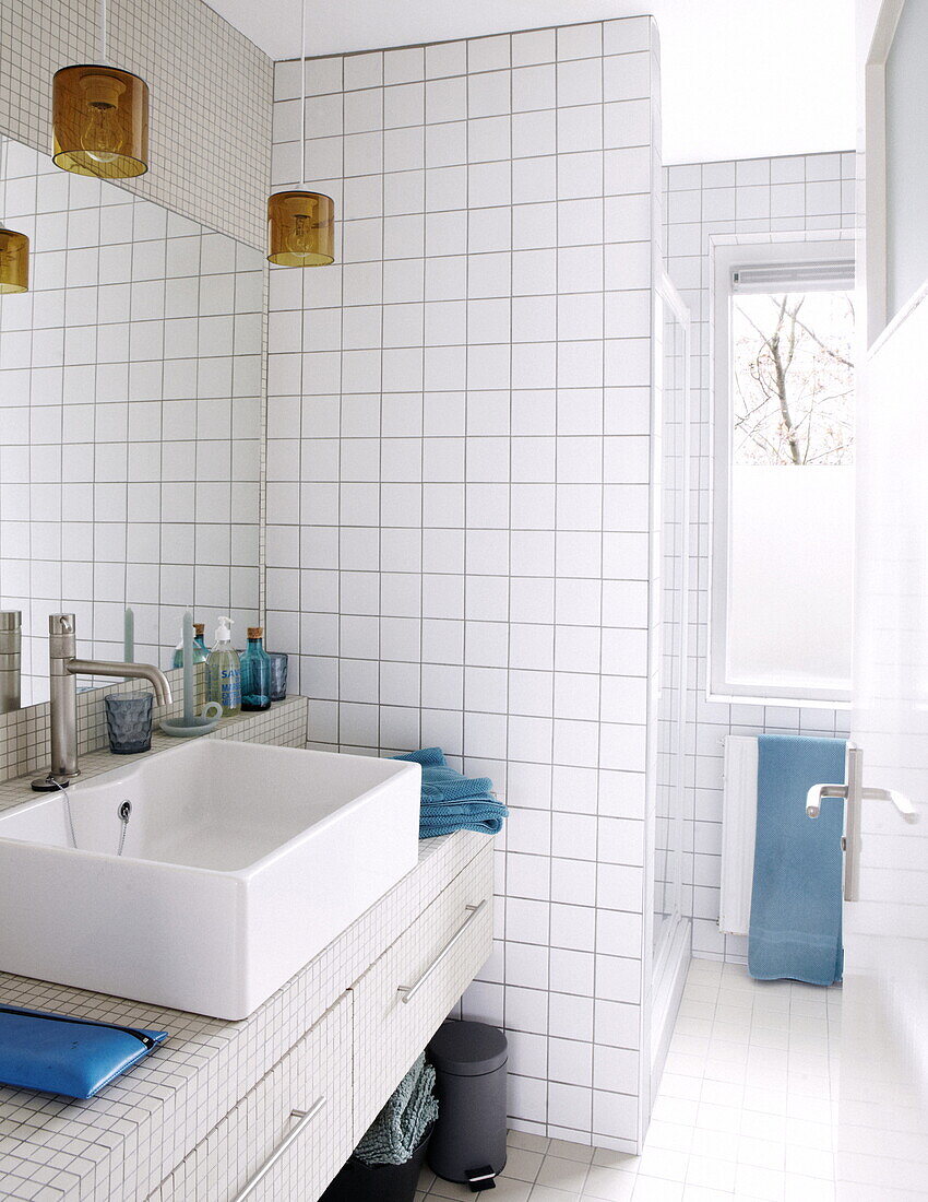 Weiß gefliestes Badezimmer mit farbigen Glaspendeln und großem Spiegel über dem Waschbecken in einem Haus in Bussum, Niederlande
