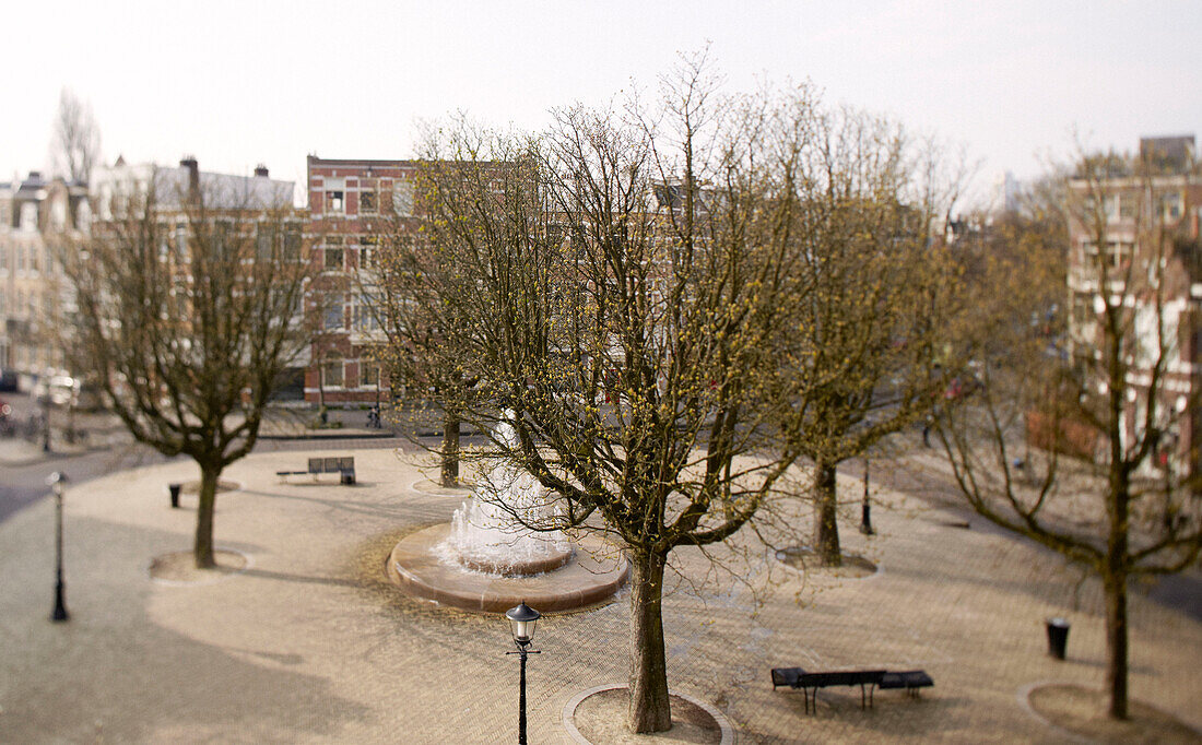 Stadtplatz mit Wasserfontäne und blühenden Bäumen in Amsterdam, Niederlande