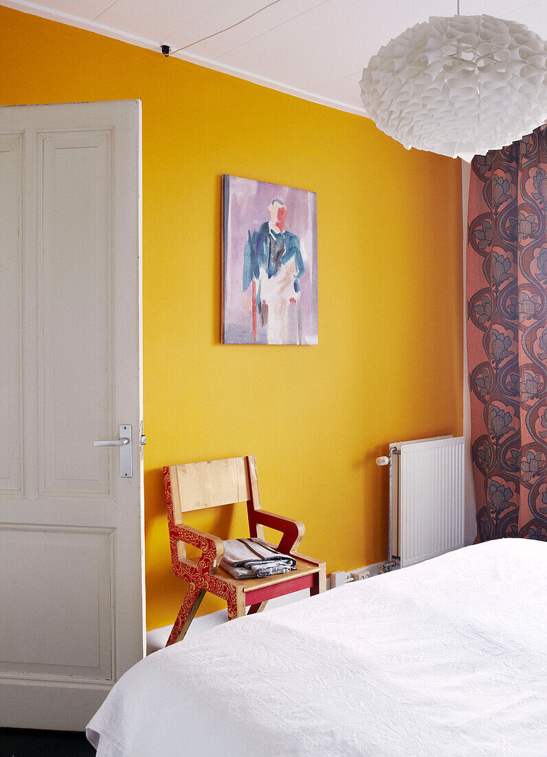 Gelbe Wand und Holzstuhl im Schlafzimmer eines modernen Familienhauses, Amsterdam, Niederlande