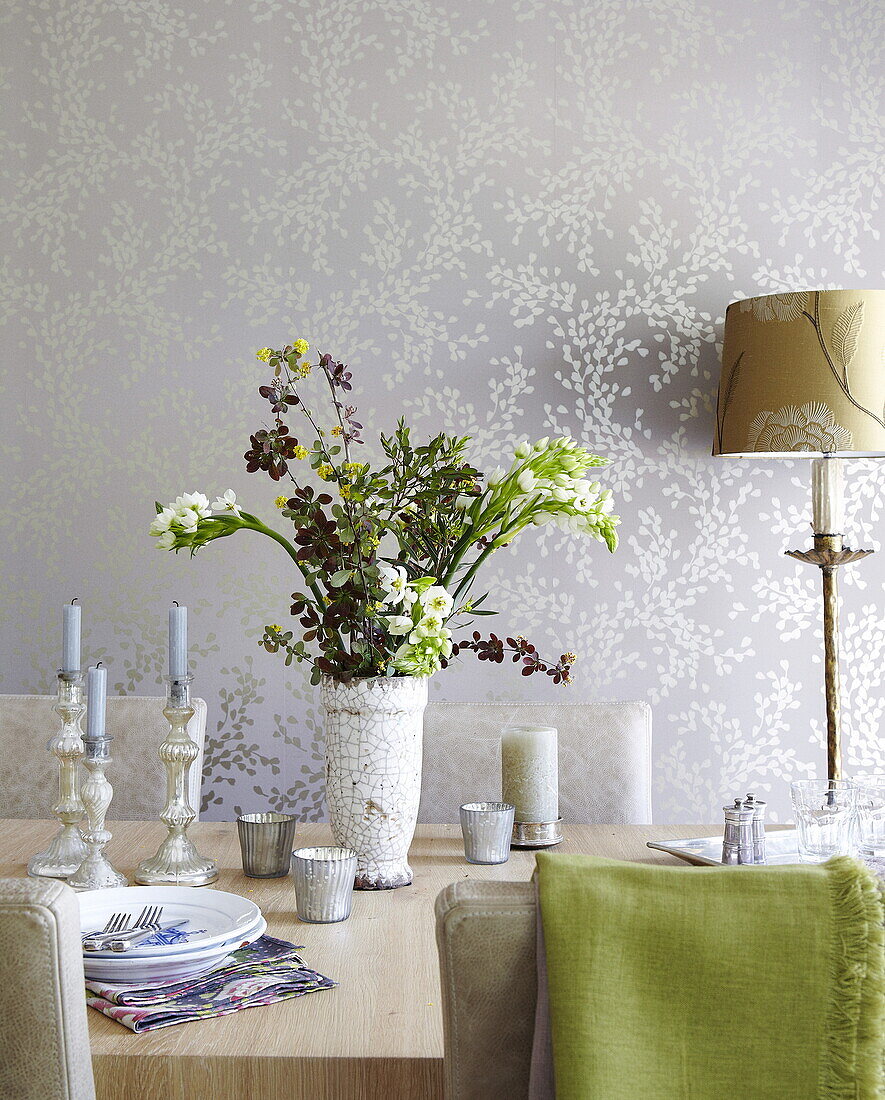 Flower arrangement on dining table in room with metallic leaf patterned wallpaper, Oxfordshire, England, UK