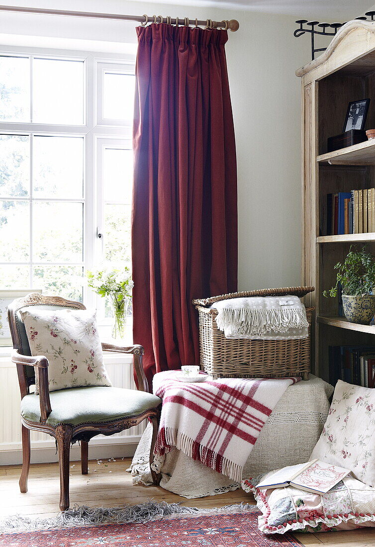 Basket and chair with bookcase at window with checked blanket, Oxfordshire, England, UK