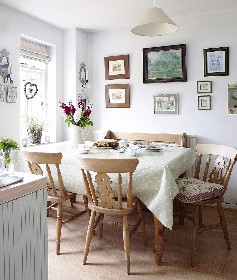 Holzstühle am Küchentisch mit gefleckter Tischdecke und an der Wand befestigtem Kunstwerk, Oxfordshire, England, UK