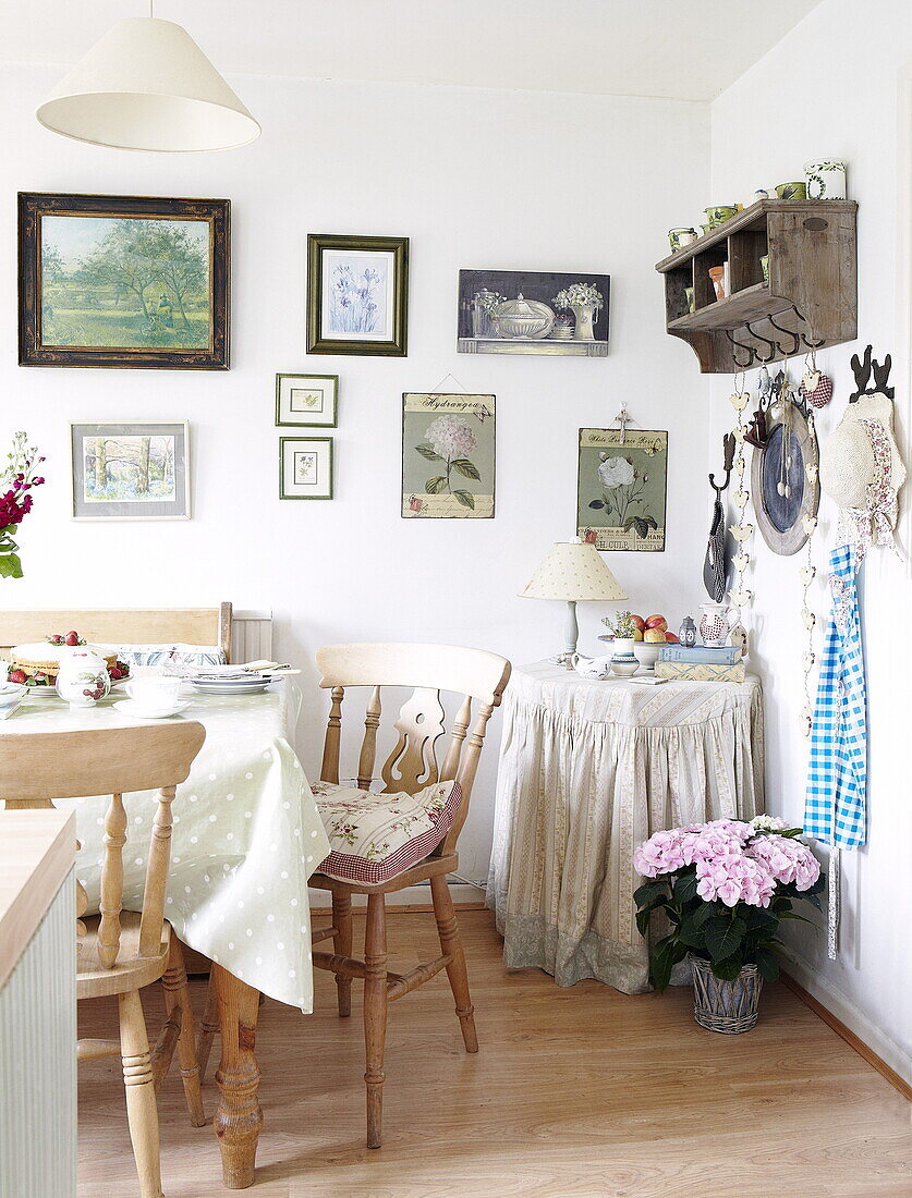 Wooden chairs at kitchen table with wall mounted artwork and shelf, Oxfordshire, England, UK
