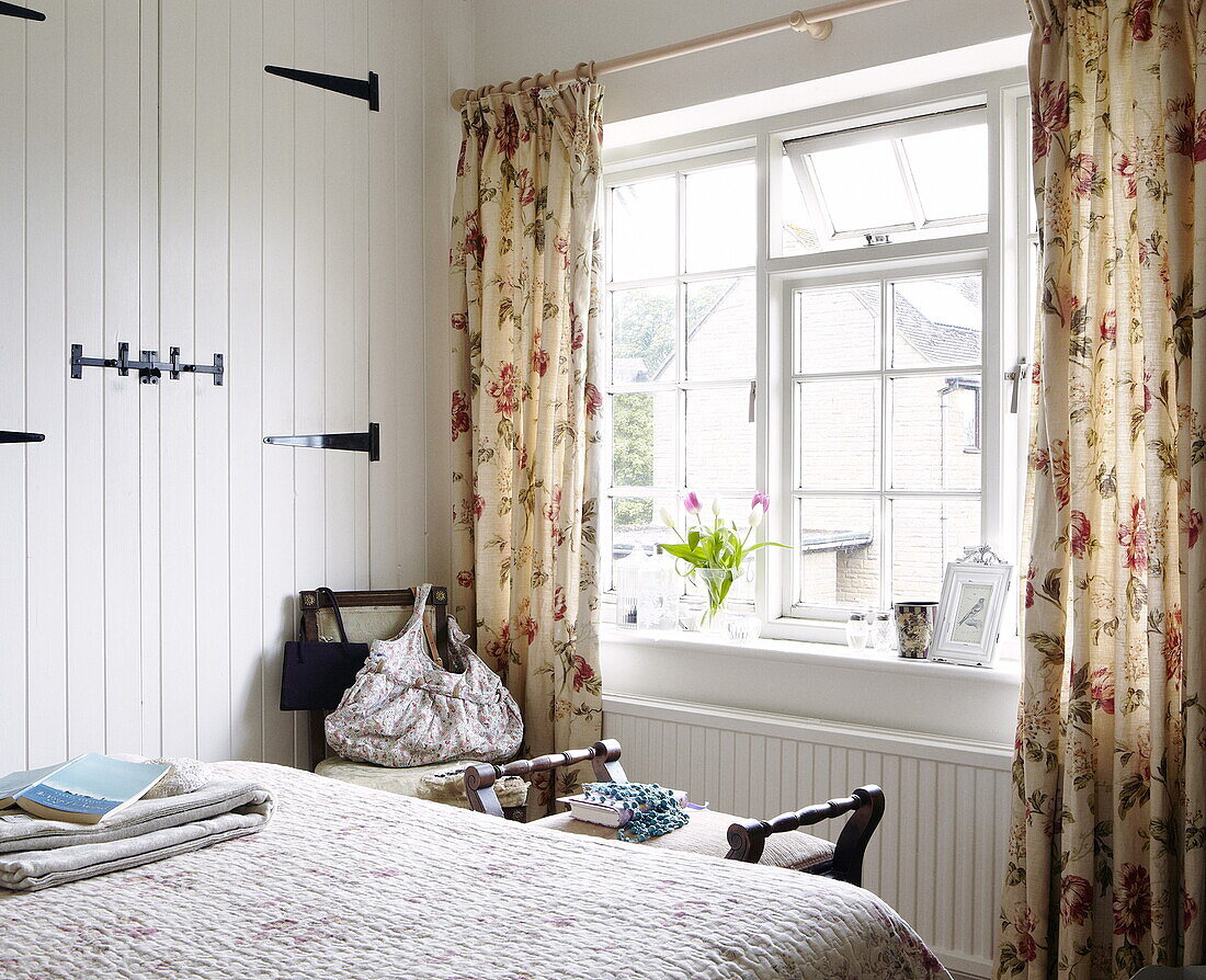 Schlafzimmer in einem Bauernhaus mit geblümten Vorhängen und Tulpen, Oxfordshire, England, UK