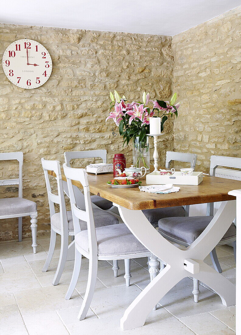 Küchentisch und -stühle mit Uhr in einem Esszimmer aus Naturstein in einer umgebauten Scheune in Oxfordshire, England, UK