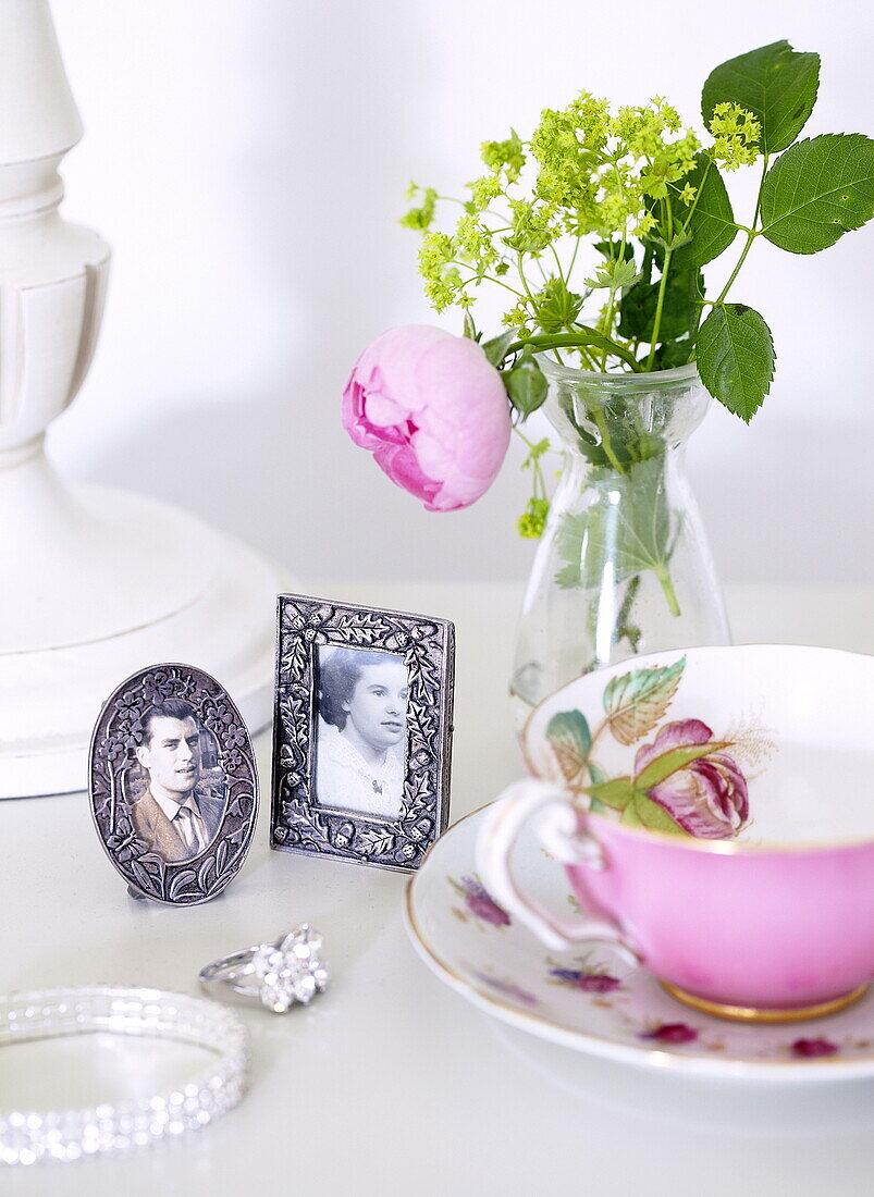 Gerahmte Fotografien und Schnittblumen mit rosa Teetasse und Verlobungsring in einem Haus in Oxfordshire, England, Vereinigtes Königreich