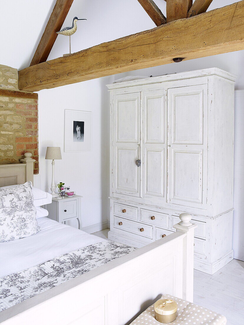 White painted wardrobe and double bed in beamed barn conversion with exposed brick wall, Oxfordshire, England, UK