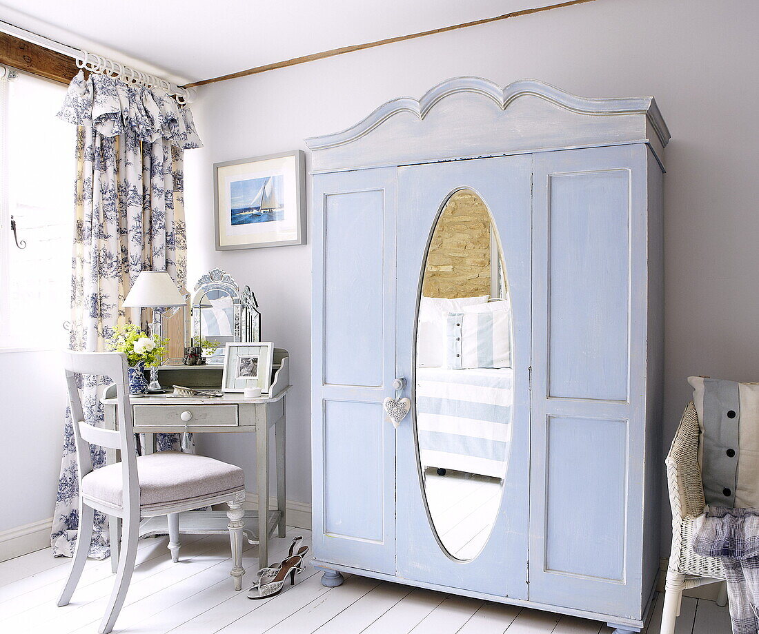 Light blue painted wardrobe with oval mirror and dressing table in bedroom in Oxfordshire, England, UK