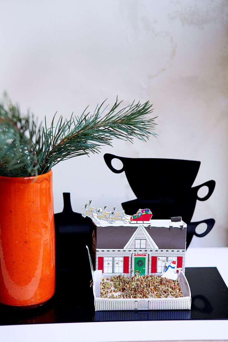 Pine needles in orange vase with cutout teacups and model house in London home England UK