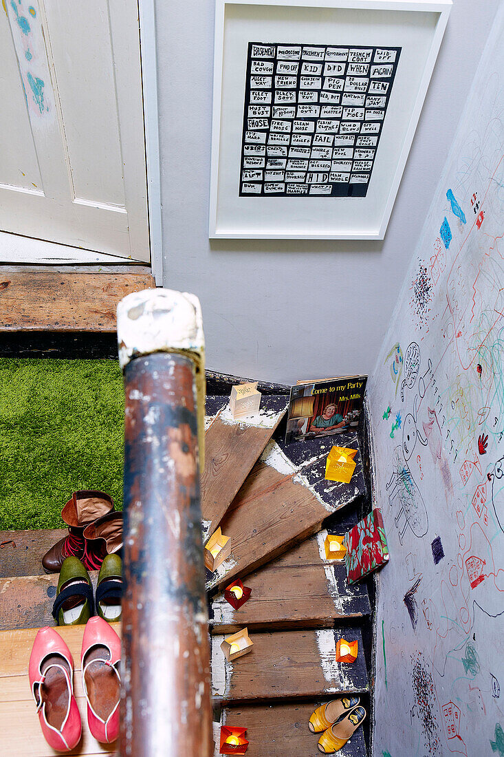 Footwear on staircase with astro-turf and child's drawings on wall of London family home England UK