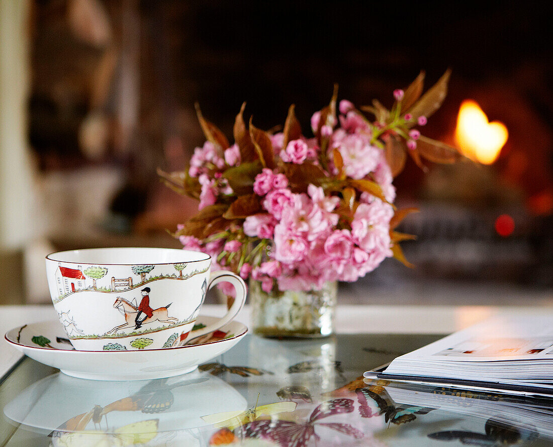 Tasse und Untertasse mit Schnittblumen auf einem gläsernen Couchtisch im Wohnzimmer eines Bauernhauses in Oxfordshire, England, UK