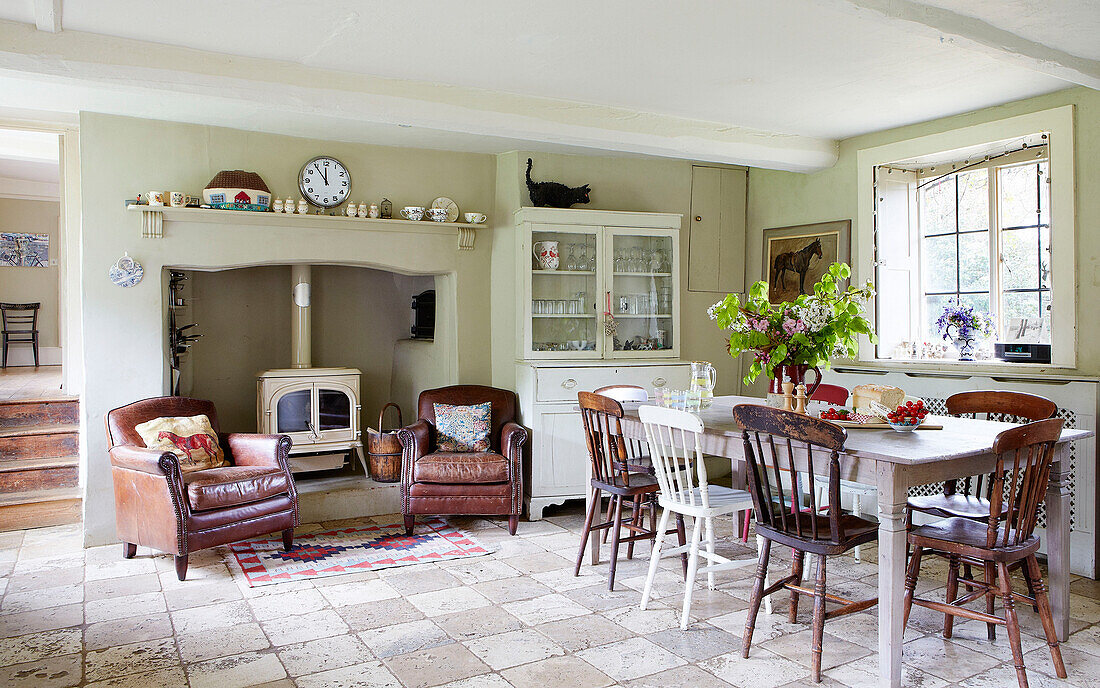 Ein Paar braune Ledersessel und ein Holzofen mit Esstisch und Stühlen in einem Bauernhaus in Oxfordshire, England, UK