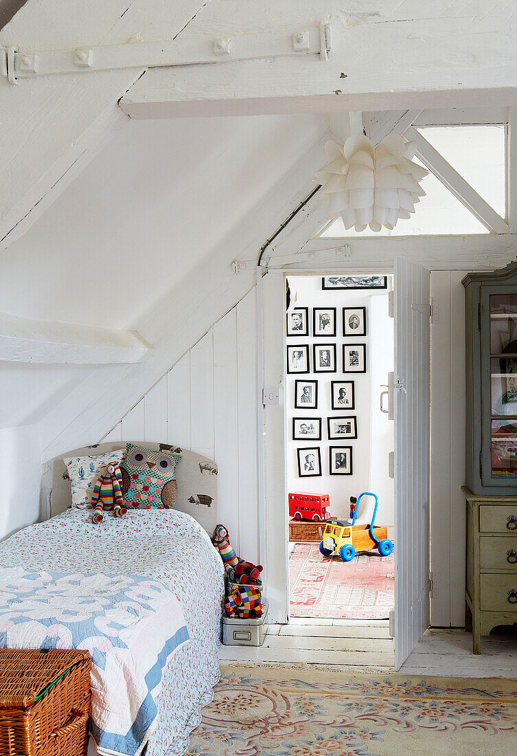 Einzelbett im Kinderzimmer mit Blick durch eine offene Tür auf eine Fotoausstellung in einem Bauernhaus in Oxfordshire, England UK