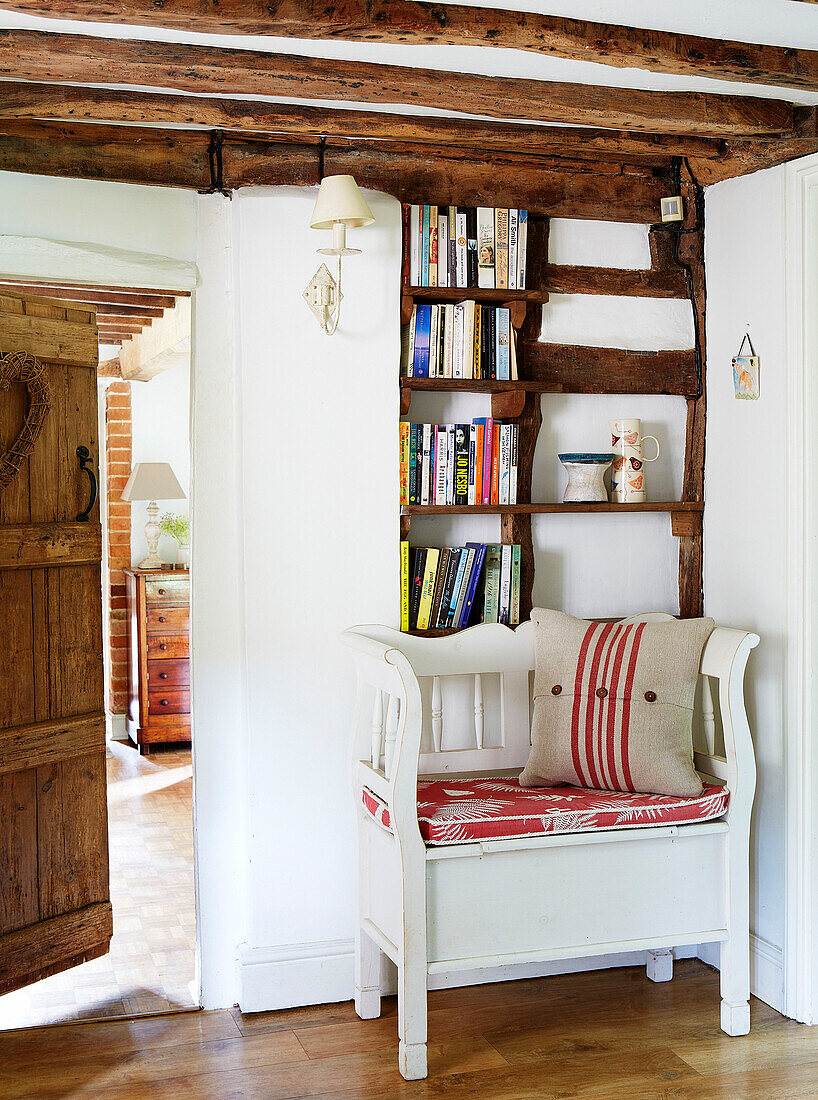 Bücherregal aus Holz und upgecycelter Sitz in einem Bauernhaus mit Balken in Surrey, England, UK