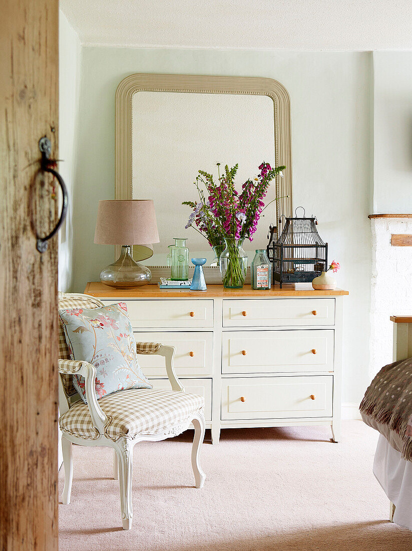 Blick durch die Schlafzimmertür auf einen karierten Stuhl und eine Kommode in einem Bauernhaus in Surrey (England)