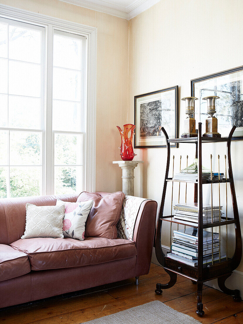 Pink leather sofa with antique display shelving in living room of London townhouse England UK