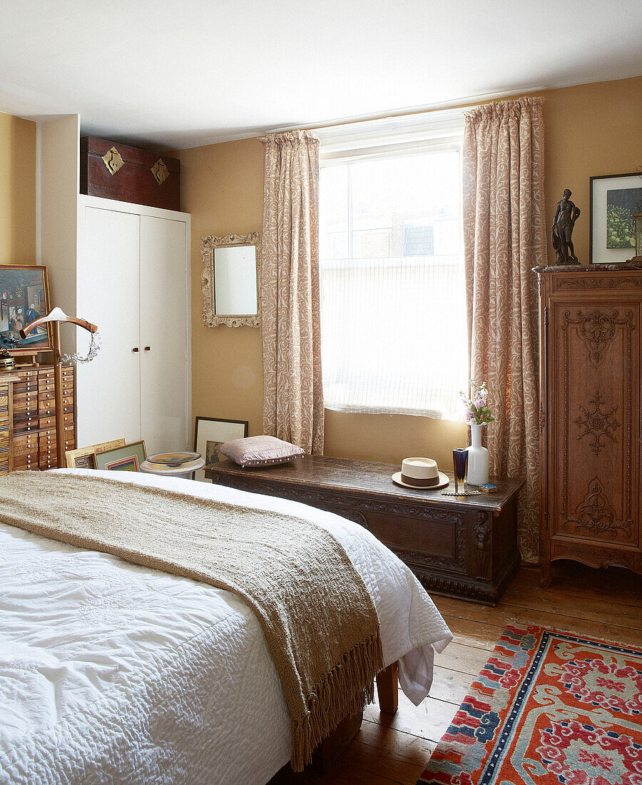Beigefarbene Decke auf weißem Doppelbett mit geschnitzten Holzmöbeln in einem Londoner Stadthaus England UK
